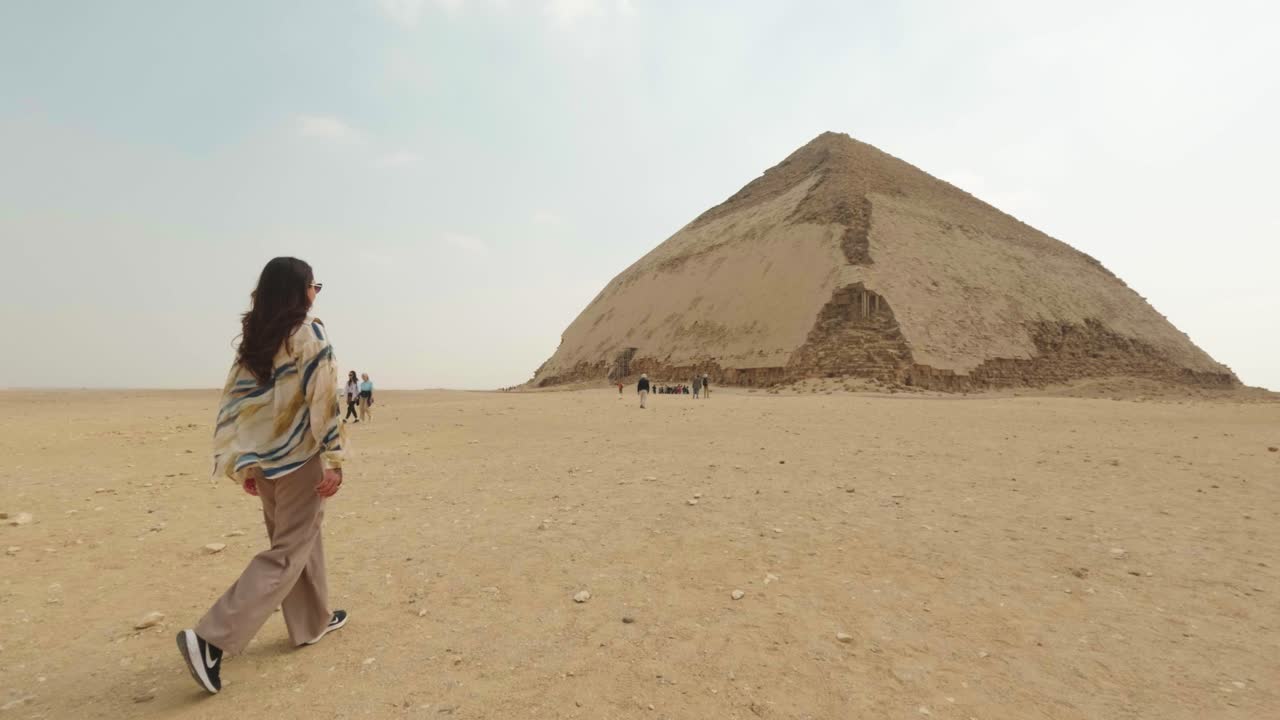 Žena kráčející ke starověké Lomené pyramidě v egyptské poušti.