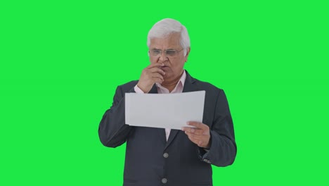 Confused-Indian-senior-manager-reading-reports-Green-screen