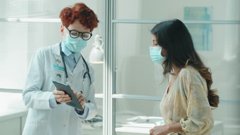 female doctor and patient in masks using tablet and speaking