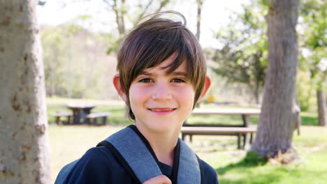 slow motion portrait of young boy with backpack in park smiling at camera