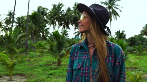 mujer pelirroja feliz con gafas de sol y sombrero en la selva tropical, vista frontal
