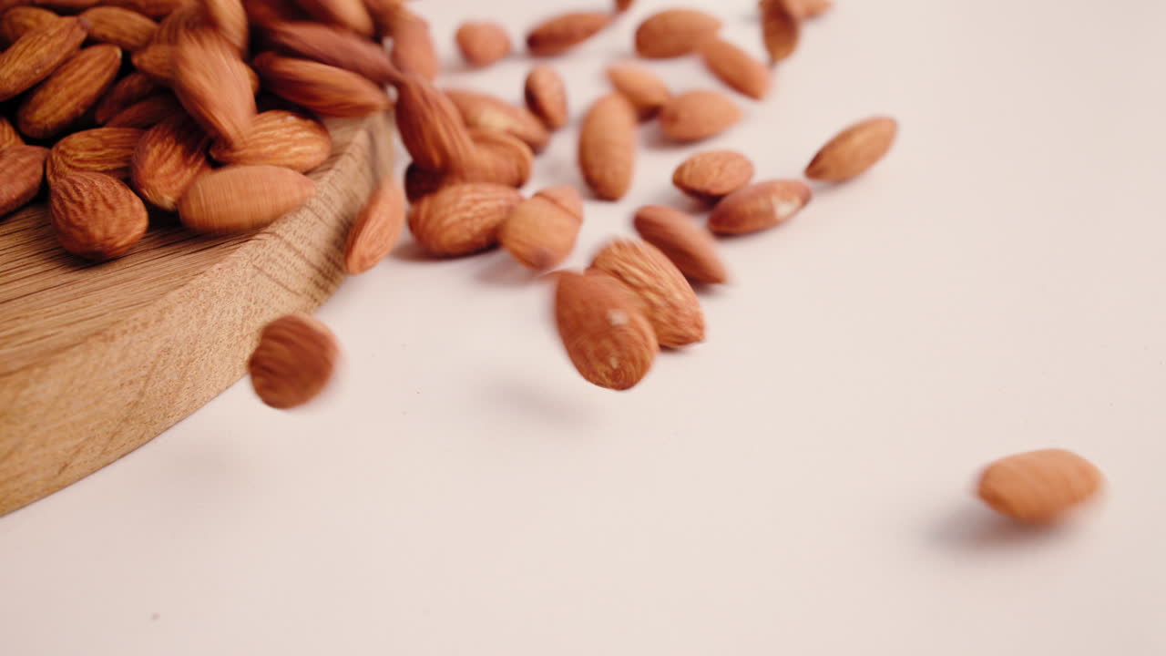 Amandes crues tombant d’une planche en bois sur un fond blanc