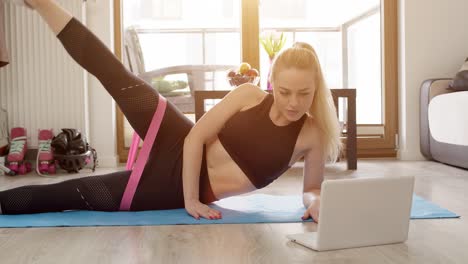 Young-sporty-beautiful-woman-exercising-at-home-in-a-living-room--Using-laptop-to-watch-online