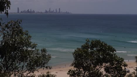 beach view with waves and surfers in water with gold coast skyline in distance. coolangatta, queensland, australia. static elevated shot