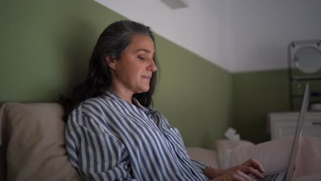 Confident-mature-Hispanic-lady-working-distantly-on-netbook-in-bed