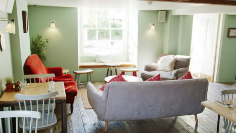 empty lounge and eating area at a pub at daytime, with armchairs, a sofa, tables and chairs in daylight and old wooden floorboards, tilt shot, pulls into focus