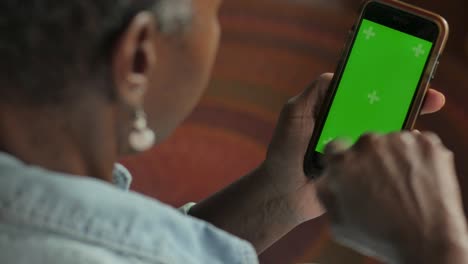 mujer afroamericana desplazándose arriba y abajo en su teléfono móvil de pantalla verde