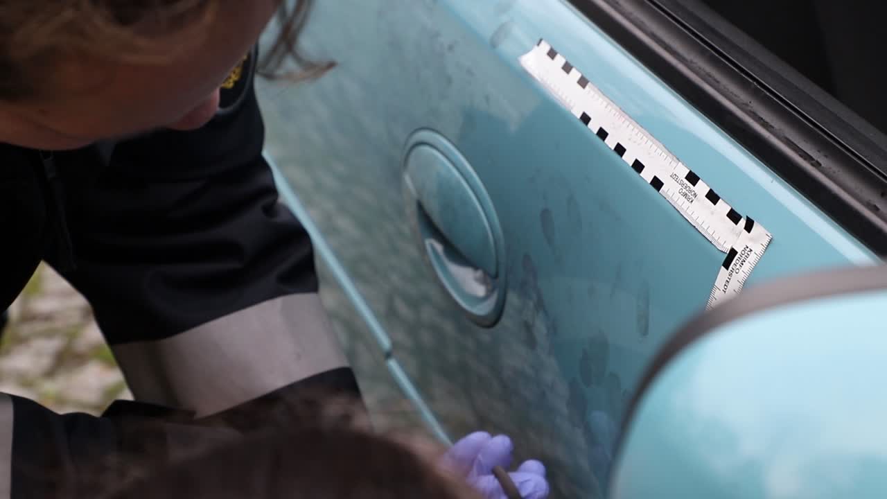Crime Scene Unit officer collecting fingerprints and evidence on a vehicle which was damaged by criminals.