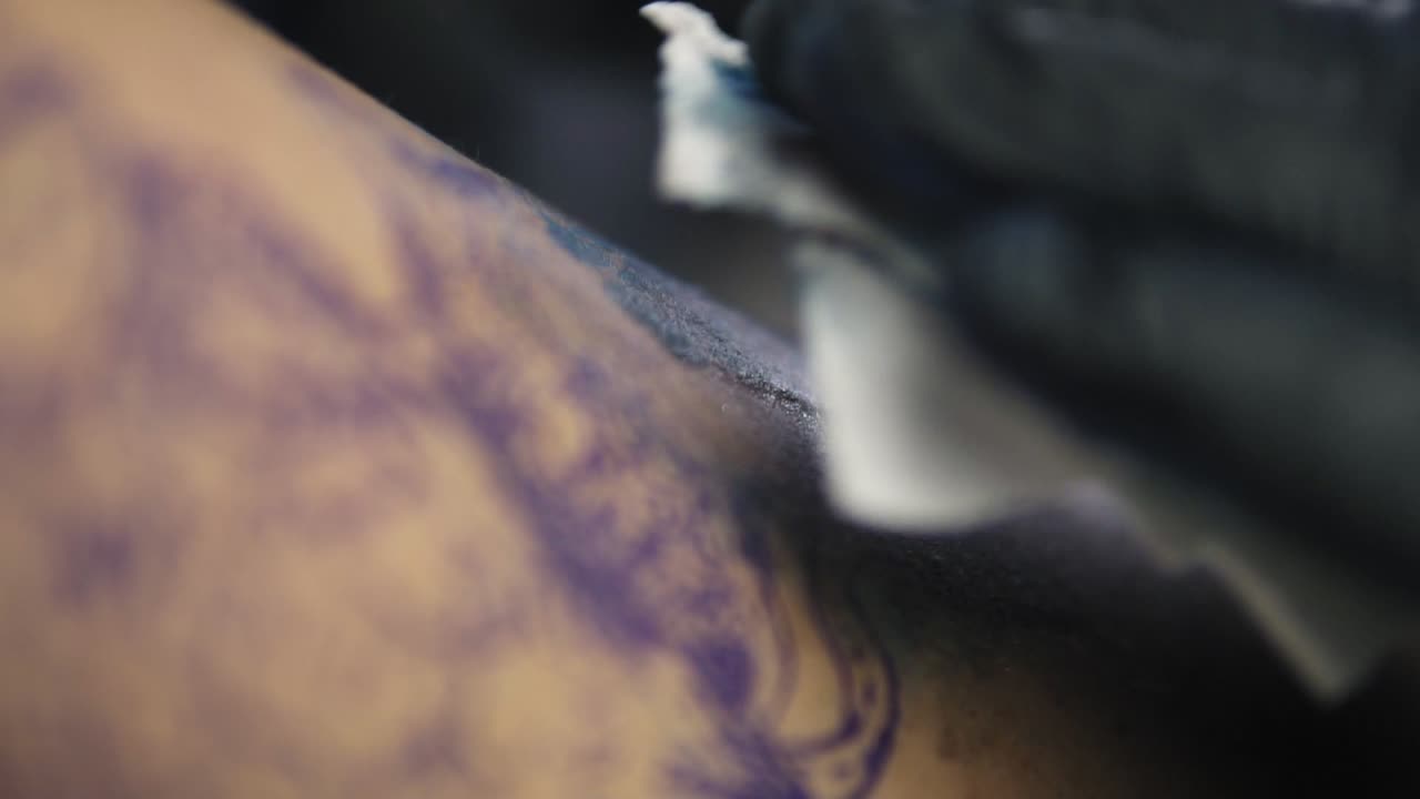 Needle tattoo machines inject a blue ink into the skin of a woman. Tattoo art on body. Makes a colorful tattoo. Professional tattooist in black gloves doing tattooing in studio. Close-up
