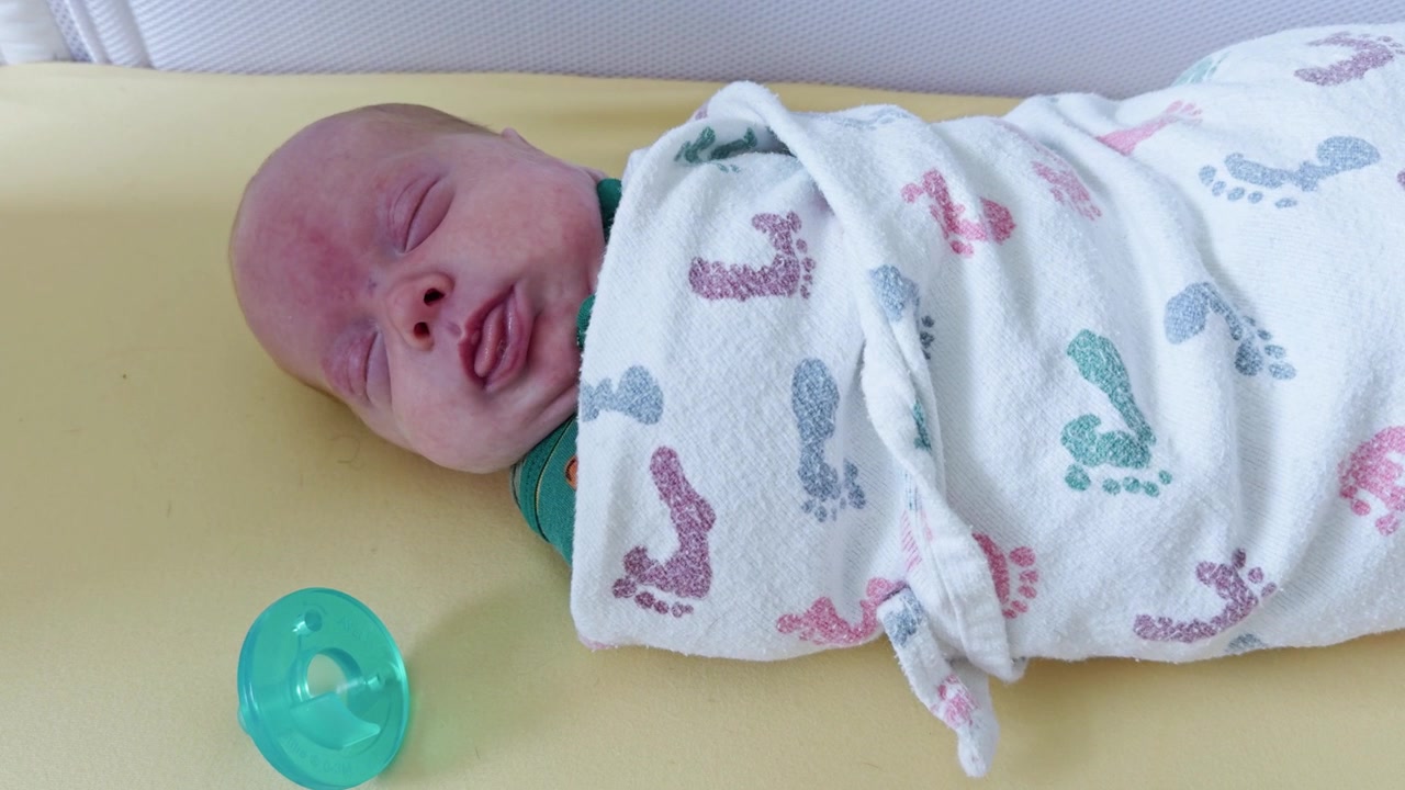 Neonato che si muove nel sonno mentre è fasciato in una culla