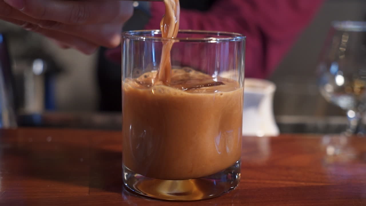Barman che versa un cocktail al caffè e cioccolato su ghiaccio in un bicchiere, riprese con slider in primo piano, slow motion 4K