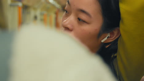 Close-Up-Of-Young-Woman-Standing-On-Underground-Train-On-Journey-To-Work-Wearing-Wireless-Earbuds