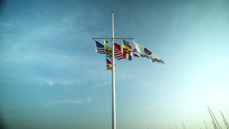 several flags for canadian provinces, the united states and other countries flap in the wind on a single flagpole