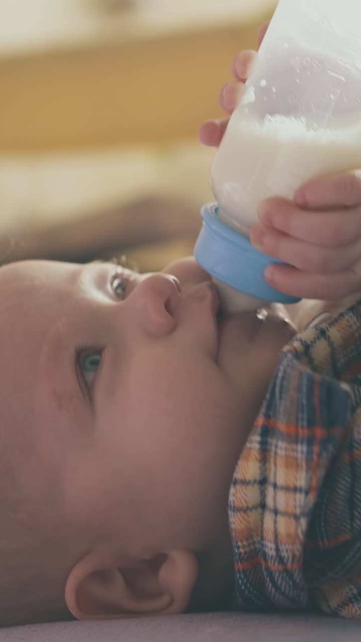 adorable little baby eats tasty milk mix from small bottle lying on soft bed in spacious light room close view