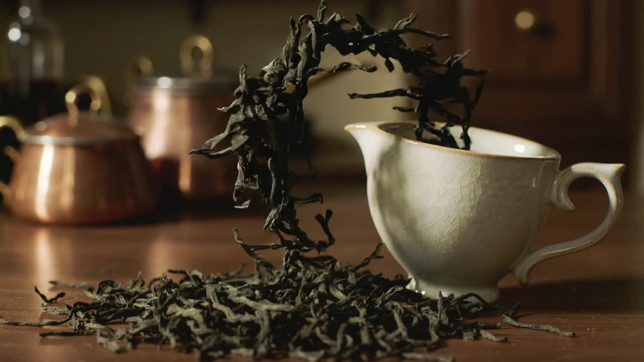 Foglie di tè scuro sfuse vengono sollevate e ricadono ad arco in una tazza bianca sul piano di lavoro della cucina, riempiendola fino all'orlo.