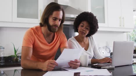 Pareja-De-Raza-Mixta-Usando-Una-Computadora-Portátil-Y-Calculando-Las-Finanzas-En-La-Cocina-De-Casa