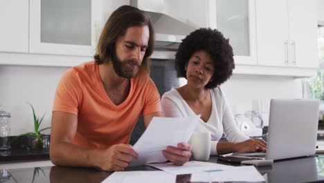 pareja de raza mixta usando una computadora portátil y calculando las finanzas en la cocina en casa