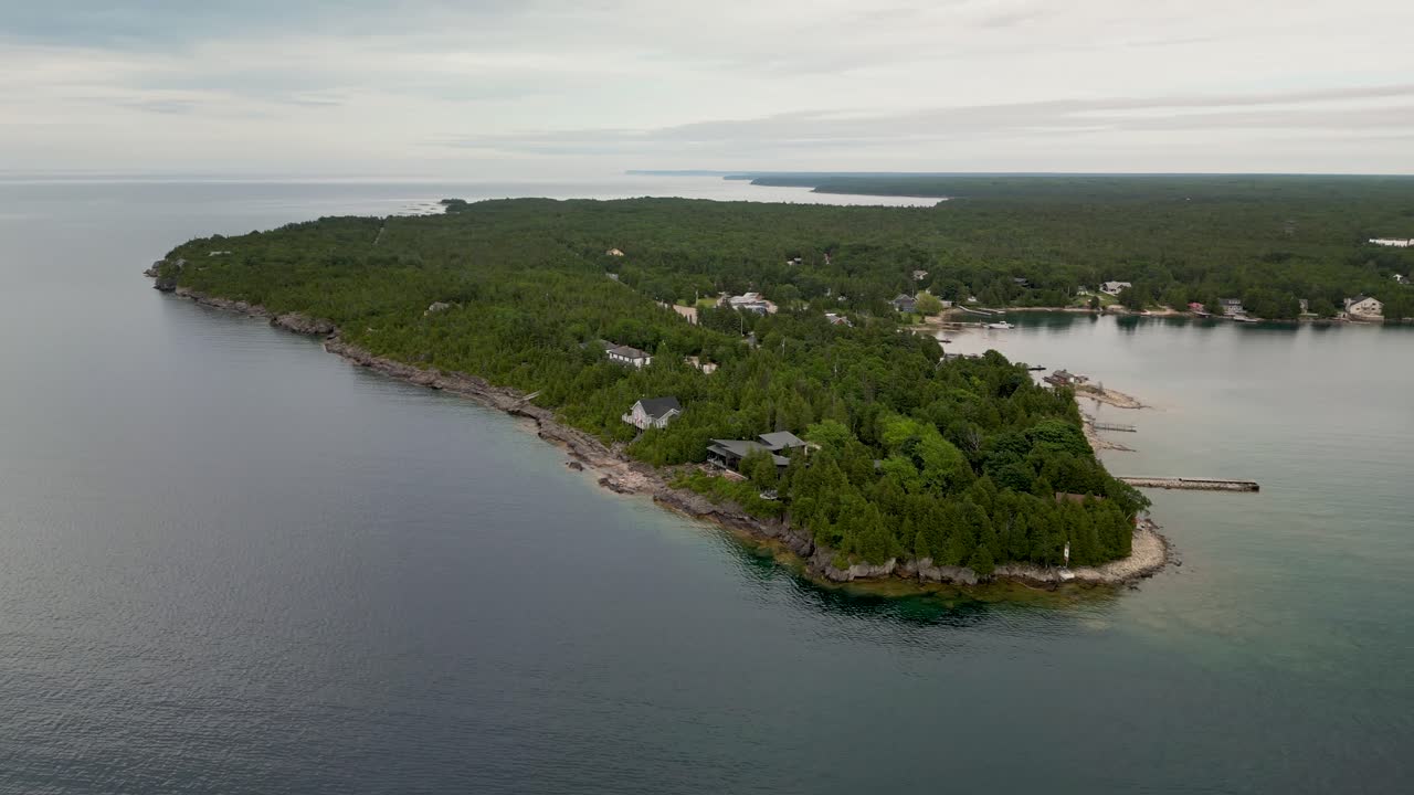 Aerial view of a forested peninsula with houses extending into a calm bay under an overcast sky