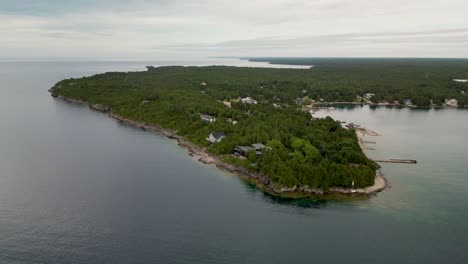 aerial view of a forested peninsula with houses extending into a calm bay under an overcast sky