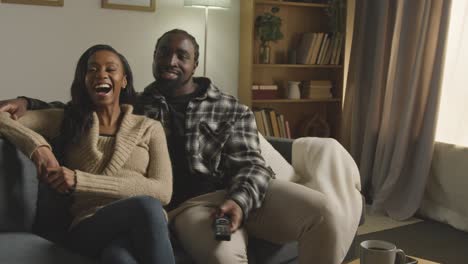 young couple relaxing at home with remote sitting on sofa watching tv together