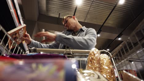 At-the-Supermarket:-Handsome-man-with-shopping-cart-uses-smartphone---talking.-Looks-at-dairy-products-and-walks-through-dry