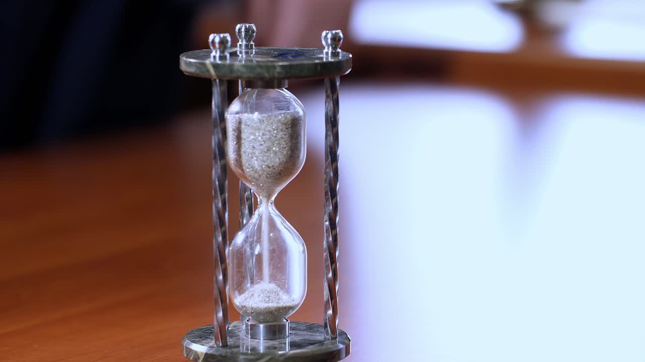 Hand holding an hourglass on a wooden desk