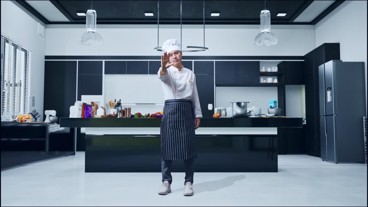 Figura intera di uno chef asiatico che guarda la telecamera e disapprova con un gesto della mano che indica "no" in una cucina di casa