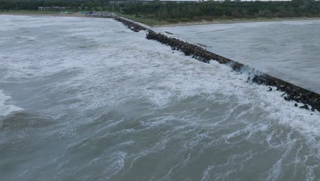 aerial establishing view of port of liepaja concrete pier , autumn storm, big waves splashing, overcast day, wide drone shot moving forward