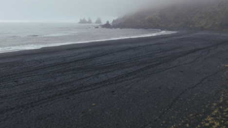 Aerial-pan-up-at-Vik-Iceland-early-winter-fog-at-Black-Sand-Beach-waves-crashing-on-shore