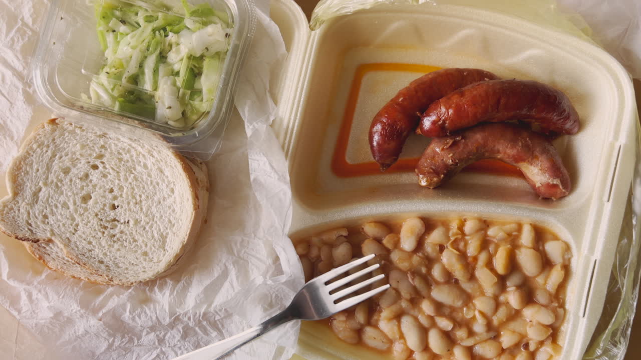 Takeaway food in styrofoam packaging - white beans and sausages with shredded cabbage salad, top view handheld footage