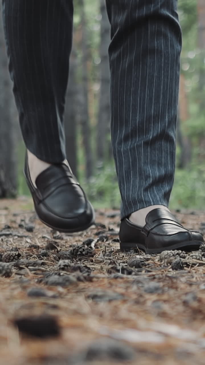 Businessman in formal suit and black shoes walks across pine forest closeup slow motion. Manager rests after stressful work in park. People and nature