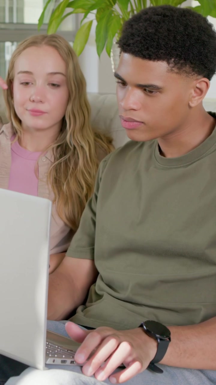 Vertical video: Glancing right, man in olive tee and smartwatch typing on laptop at home, working