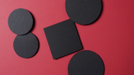 Video-of-close-up-of-square-and-circles-of-black-paper-and-copy-space-on-red-background