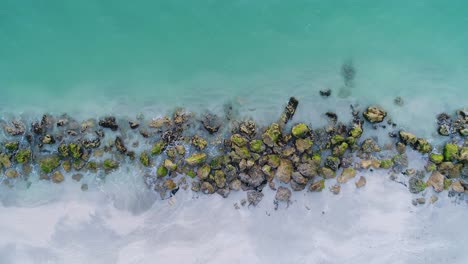 splashing blue ocean water among rocks covered in algae along the seashore aerial crane