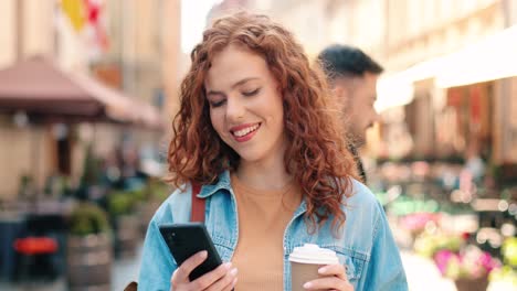 Mujer-Pelirroja-Sosteniendo-Café-Para-Llevar-Y-Usando-Un-Teléfono-Inteligente-En-La-Calle