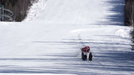 Red-snow-groomer-towing-a-group-of-skiers-up-a-snowy-ski-slope,Czechia