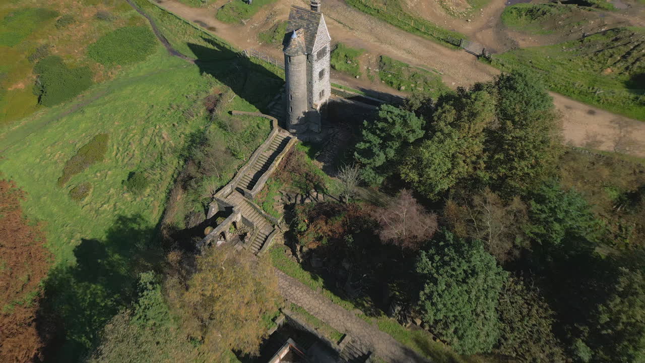 언덕 위에 있는 외로운 돌탑 건물, 빠른 날아가는 주변 시골과 언덕을 드러낸다.