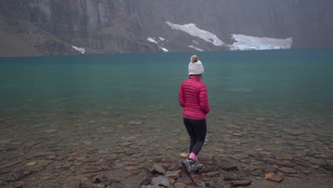 mujer en la costa del lago iceberg, parque nacional glaciar, montana, estados unidos en el frío día de otoño, cámara lenta