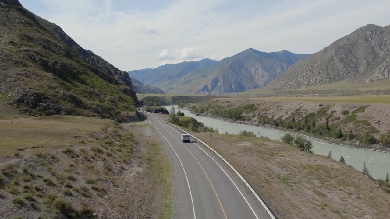 Imágenes de dron de un vehículo circulando por el Chuysky Trakt junto al río Katún, rodeado por las escarpadas montañas de Altai y un amplio paisaje de valle, República de Altai, Rusia