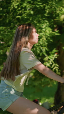 vista lateral de una mujer joven que anda con confianza en bicicleta a través de un parque verde exuberante, su largo cabello fluye detrás de ella, expresando una determinación tranquila, el fondo muestra vegetación y sombras suaves