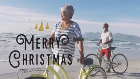animación de texto de feliz navidad sobre una feliz pareja de ancianos diversa con bicicletas en una playa soleada.