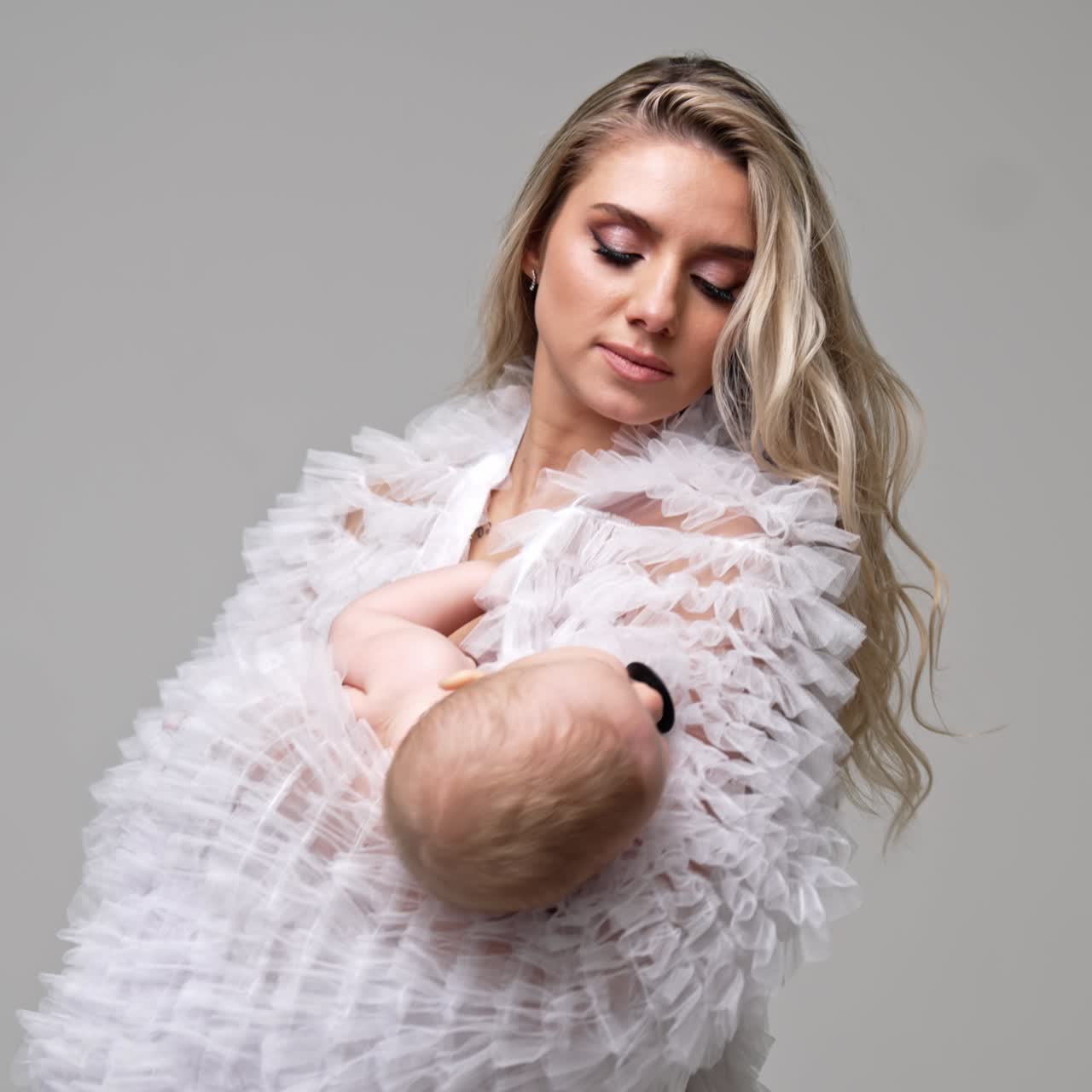 Donna con capelli lunghi in veste bianca che tiene in braccio un bambino. Mamma premurosa che culla il suo bambino per farlo addormentare