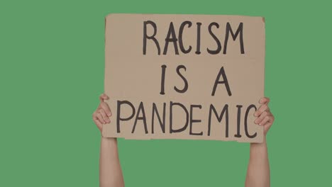 hands hold a poster with the slogan racism is a pandemic against the background of a green screen, chroma key. stop racism concept, no racism. close up. slow motion