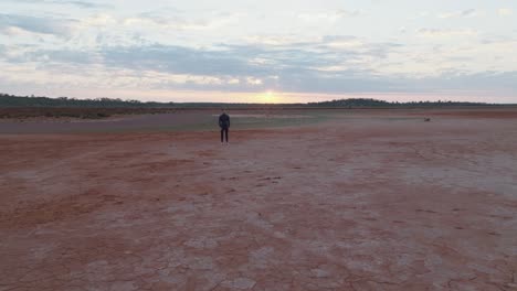 Drohnenclip,-Der-Sich-Auf-Ein-Männliches-Model-Im-Neoprenanzug-Zubewegt,-Das-Im-Outback-Westaustraliens-Steht