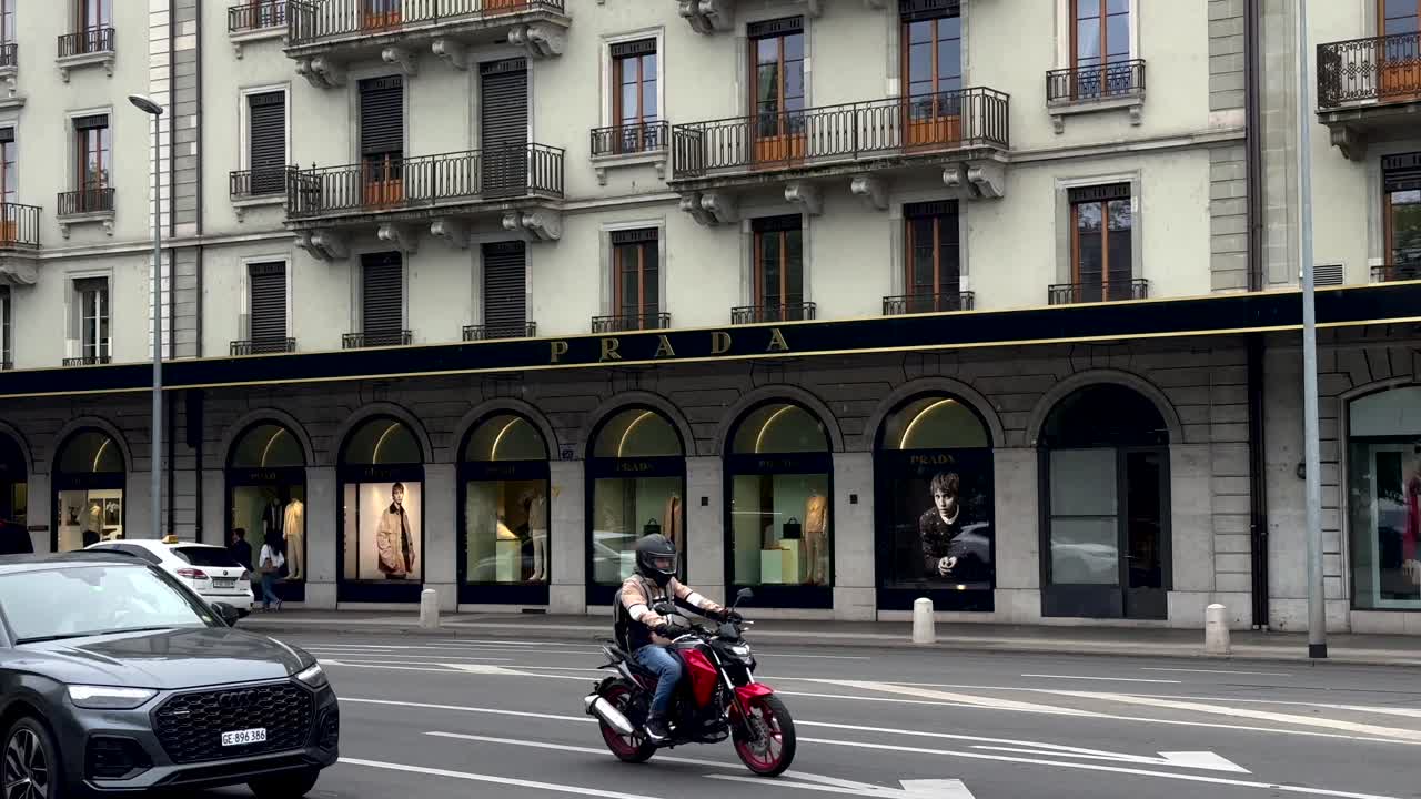Rainy day in Geneve City with Prada Shop and traffic on street. Slow motion wide shot in Switzerland. Luxury shop storefront. Pedestrian Walking on sidewalk.