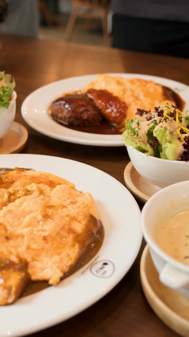 Creamy omelette rice, salad, soup, and hamburger steak arranged on wooden table, natural lighting