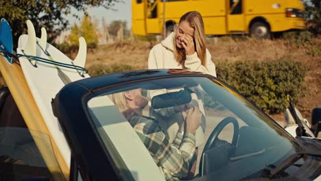 Ein-Blondes-Mädchen-In-Einem-Weißen-Sweatshirt-Kommuniziert-Mit-Ihrem-Blonden-Freund-Mit-Bart-Und-Kariertem-Hemd,-Der-In-Einem-Weißen-Cabrio-Mit-Surfbrettern-In-Der-Stadt-Sitzt