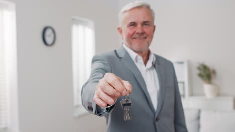 shot of apartment keys extended on palm of hand toward camera, gray-haired mature man dressed in suit hands over keys, real estate agent, owner of apartment, gives room to use