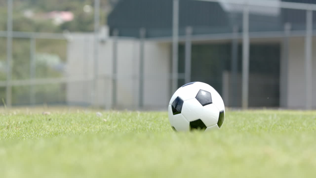 Fodbold på græsbane nær skolebygning, klar til kamp, med plads til tekst.