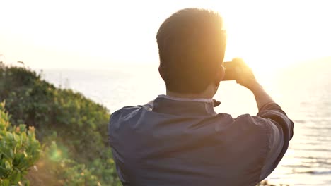 a happy young man or traveler taking a picture of a sunset on his cellphone or smartphone.